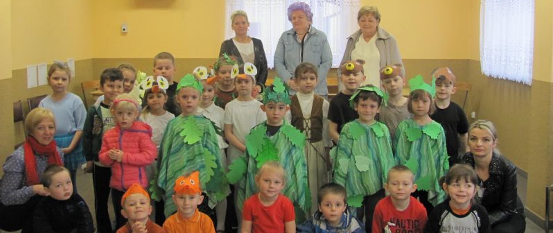 Grupa dzieci z opiekunkami w strojach do spektaklu Jarzębinka, za nimi stoją trzy panie.