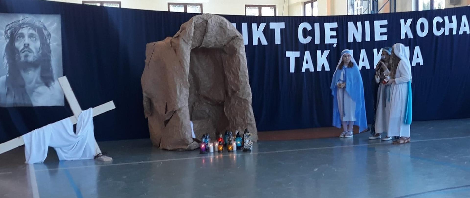 Dekoracja inscenizacji wielkanocnej, w tle grota i krzyż oraz napis "NIKT CIĘ NIE KOCHA TAK JAK JA"