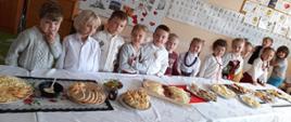 Zdjęcie przedstawia przedszkolaków ubranych w stoję góralskie, stojące za stołem na którym znajdują się produkty regionalne przygotowane do poczęstunku w sali przedszkola