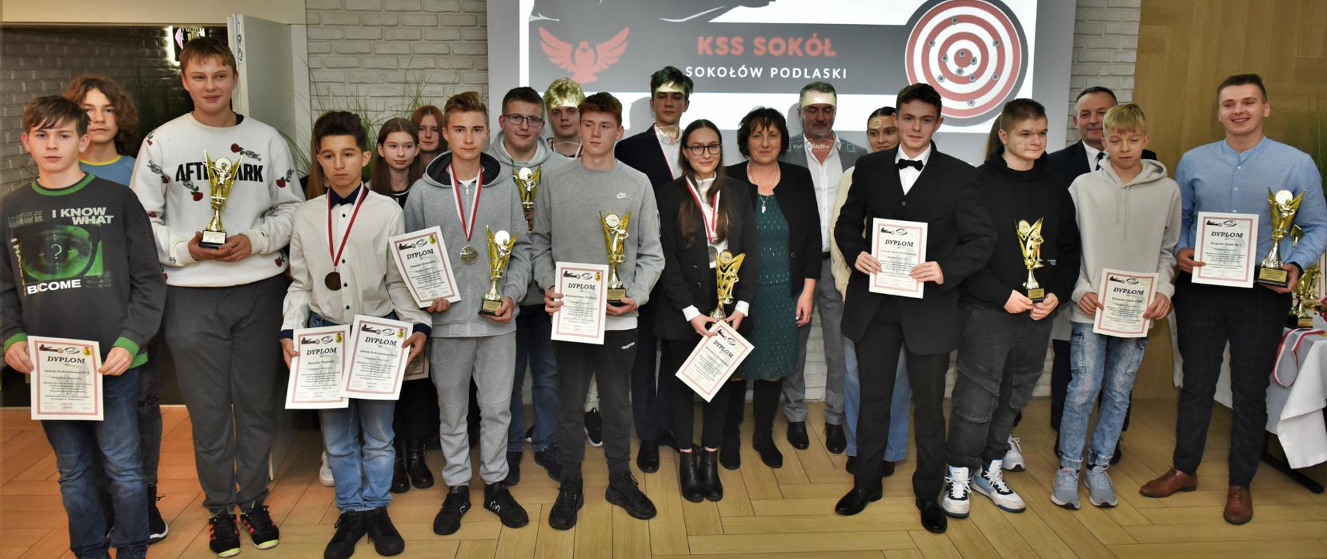 Zdjęcie grupowa, na którym starosta Sokołowski Elżbieta Sadowska stoi wraz ze zwycięzcami zawodów. Młodzież trzyma w rękach puchary i dyplomy, a na szyjach zawieszone są medale.