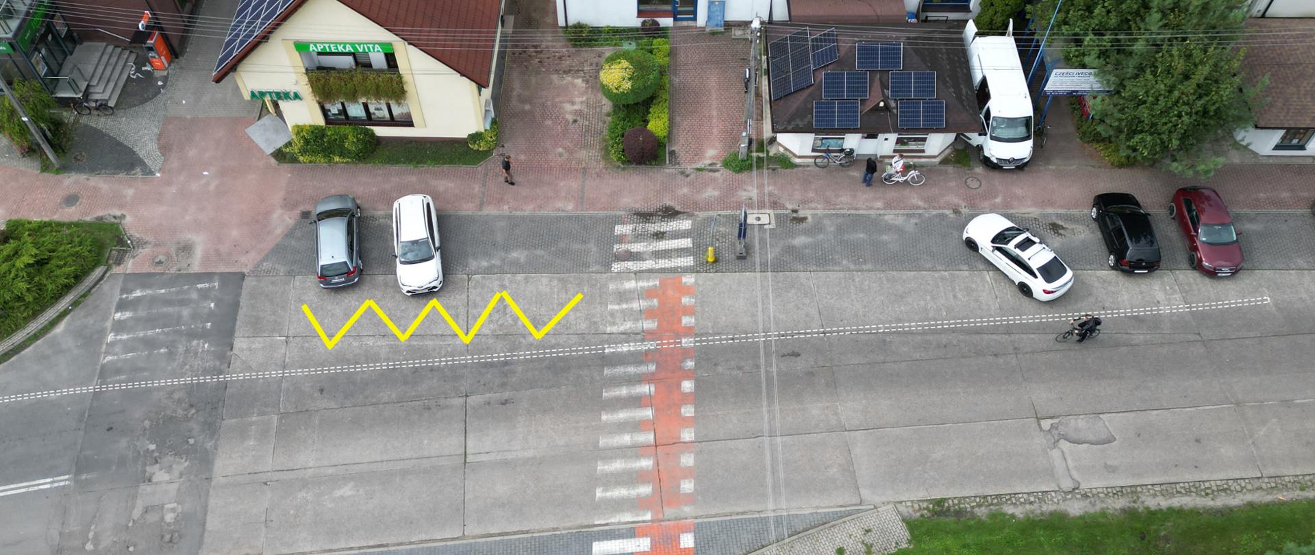 Droga przy której stoją zaparkowane samochody z zaznaczonym przejściem dla pieszych.