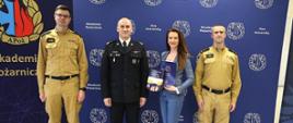 Zdjęcie starosty zambrowskiego Edyty Marchlskiej-Groszfeld wraz z dwoma mężczyznami w piaskowych mundurach strażackich oraz oficerem straży pożarnej w ciemnym mundurze. 