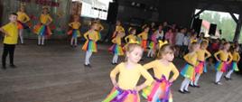 zdjęcie przedstawia małe dziewczynki w kolorowych strojach tańczące wspólny taniec 