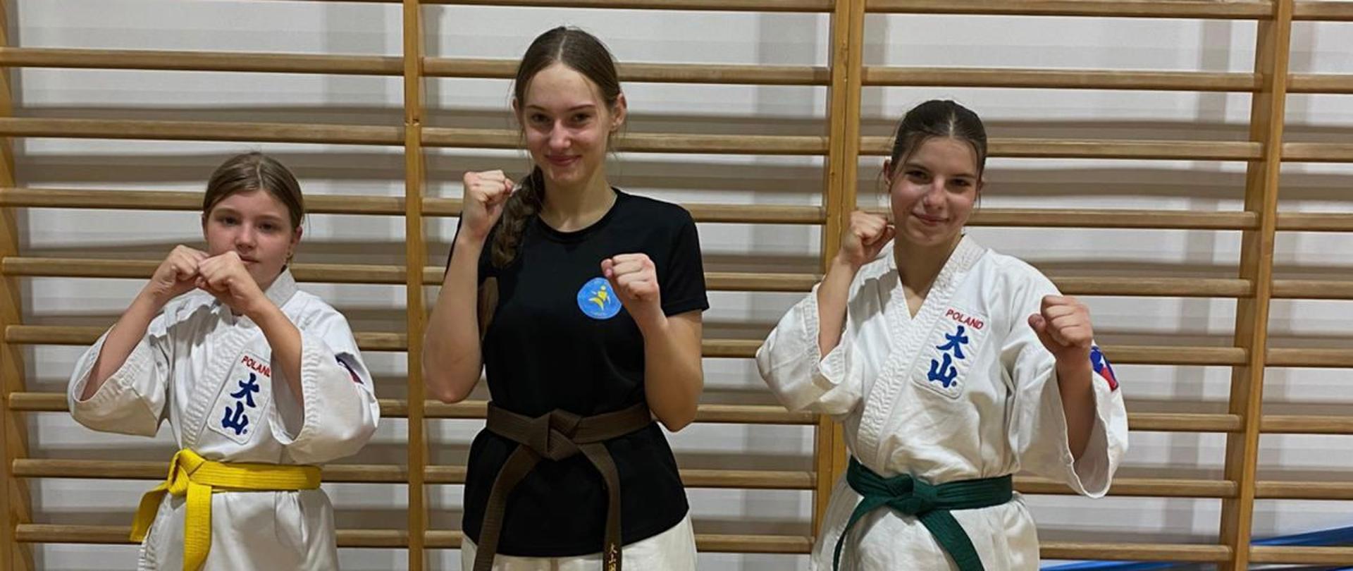 Dziewczyny w strojach karateków pozują do zdjęcia na sali sportowej