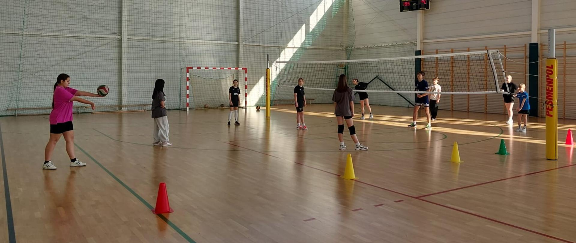 Grupa młodzieży grająca w siatkówkę na hali sportowej podczas ferii. 