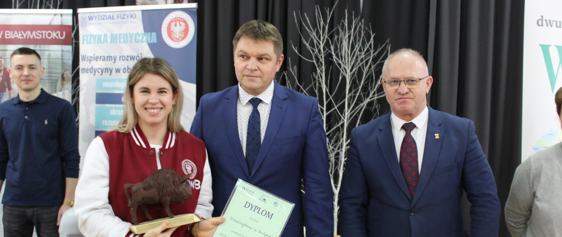 Przedstawicielka Politechniki Białostockiej odbiera nagrodę Starosty Hajnowskiego - obok niej do zdjęcia pozują Starosta Hajnowski i Zastępca Burmistrza Miasta Hajnówka