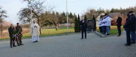 Przemawiający Wójt Gminy Ruda Maleniecka – Pan Leszek Kuca na placu przed Obeliskiem, w tle mieszkańcy i Ks. Proboszcz.