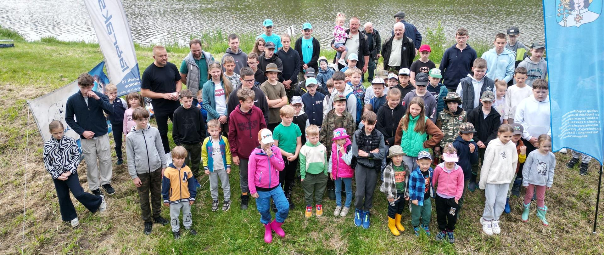 Grupa dzieci pozuje do zdjęcia na grobli stawu