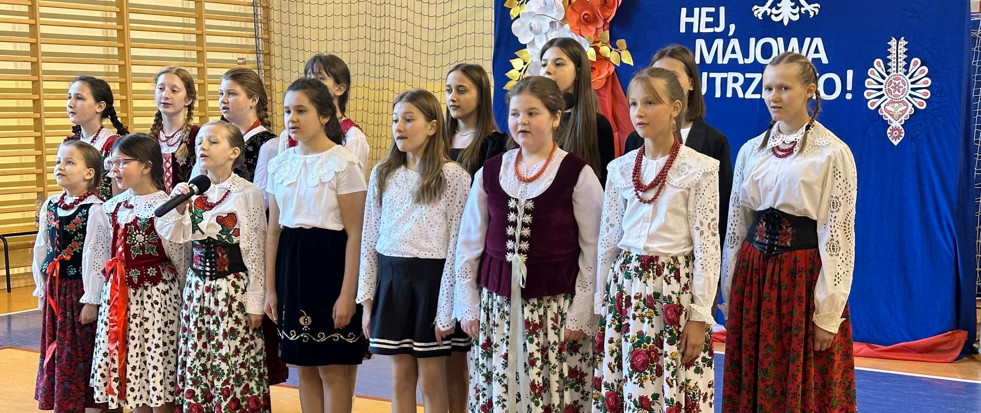 Zdjęcie przedstawia na sali gimnastycznej szkoły podstawowej w Rokicinach Podhalańskich uczniów przedstawiający patriotyczny program artystyczny na Obchody Święta Konstytucji 3 Maja.