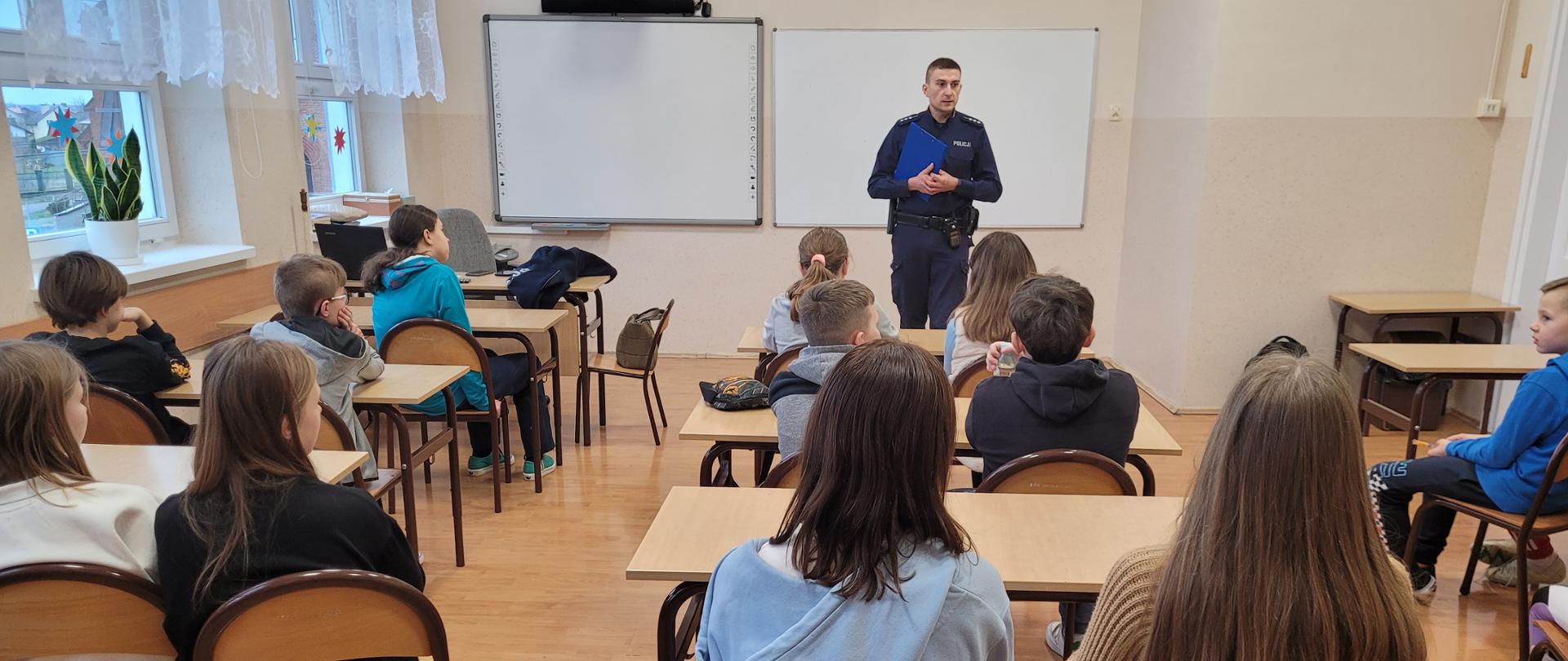 Policjant w sali lekcyjnej prowadzi prelekcję z uczniami klas starszych.