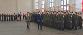 Na zdjęciu wicepremier przechodzi koło stojących na baczność oddziałów w towarzystwie ucznia - dowódcy uroczystości.