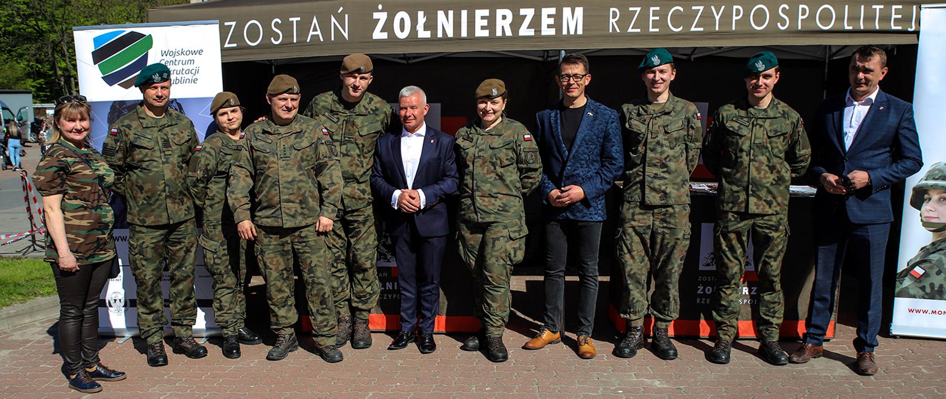 Zdjęcie przedstawia wojskowych w mundurach oraz przedstawicieli Powiatu Kraśnickiego stojących w rzędzie. Za nimi znajduje się namiot, na którym znajduje się napis "Zostań żołnierzem Rzeczypospolitej".