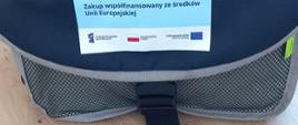 Zdjęcia przedstawia drewniany blat, na którym znajduje się czarna torba, na środku której znajduje się niebieska naklejka - fundusze europejskie, zakup współfinansowany z środków Unii Europejskiej. poniżej znajdują się logotypy.
