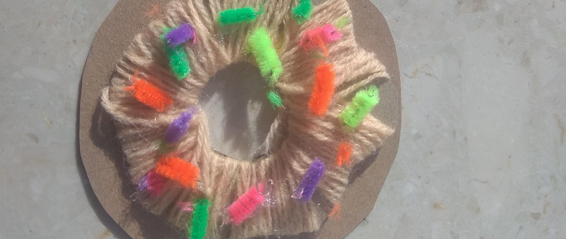 Na szarym stole dwa pączki wykonane z włóczki