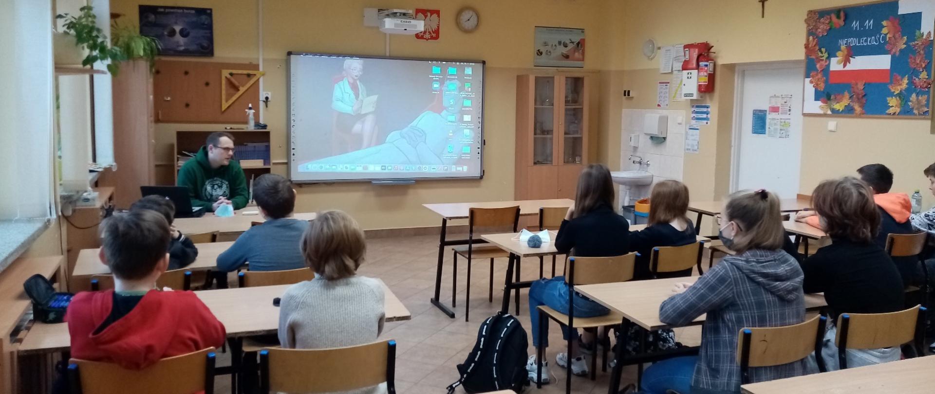 Dzieci siedzą w klasie i oglądają prezentację