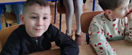 Przedszkolaki siedzą w ławkach szkolnych