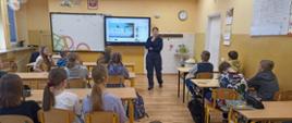 Uczniowie siedzą w ławkach i słuchają pogadanki przeprowadzanej przez panią policjantkę