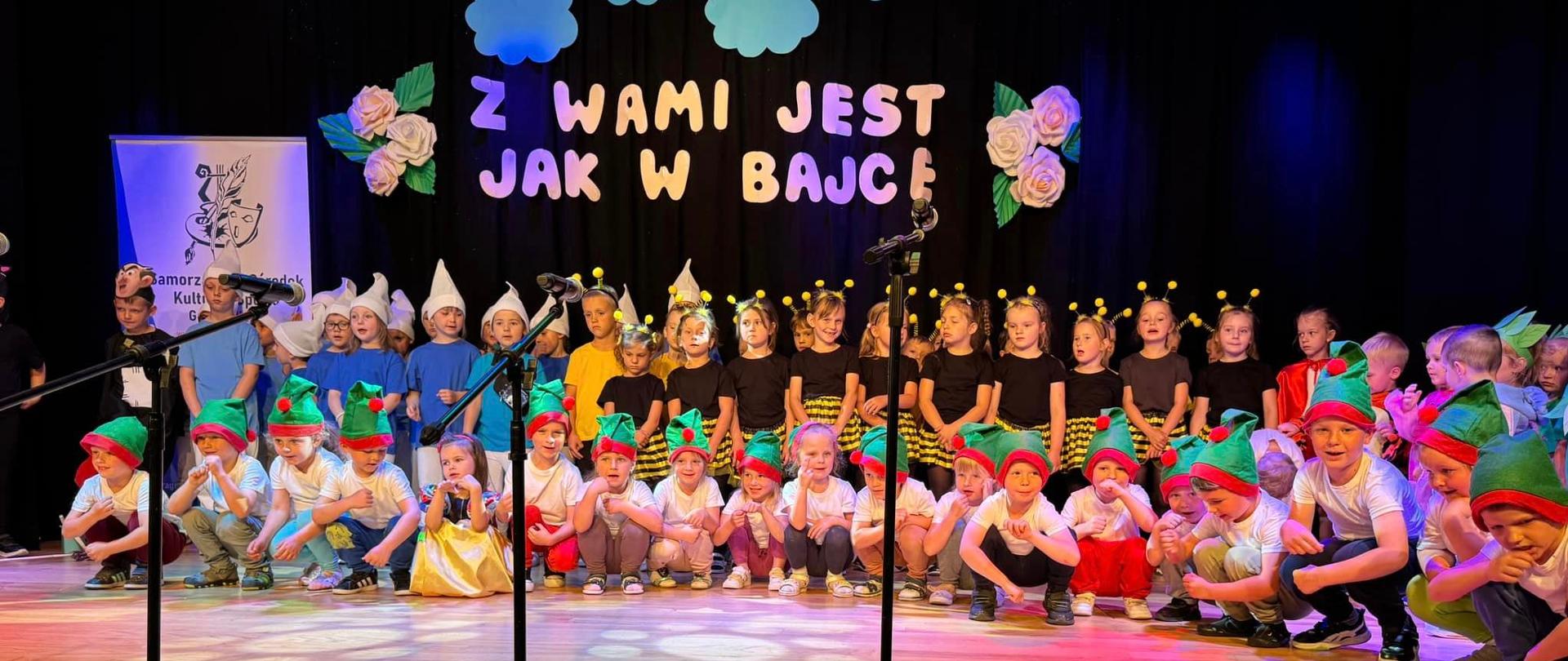 Dzieci na scenie w kolorowych strojach występują podczas uroczystości z okazji Dnia Mamy i Taty
