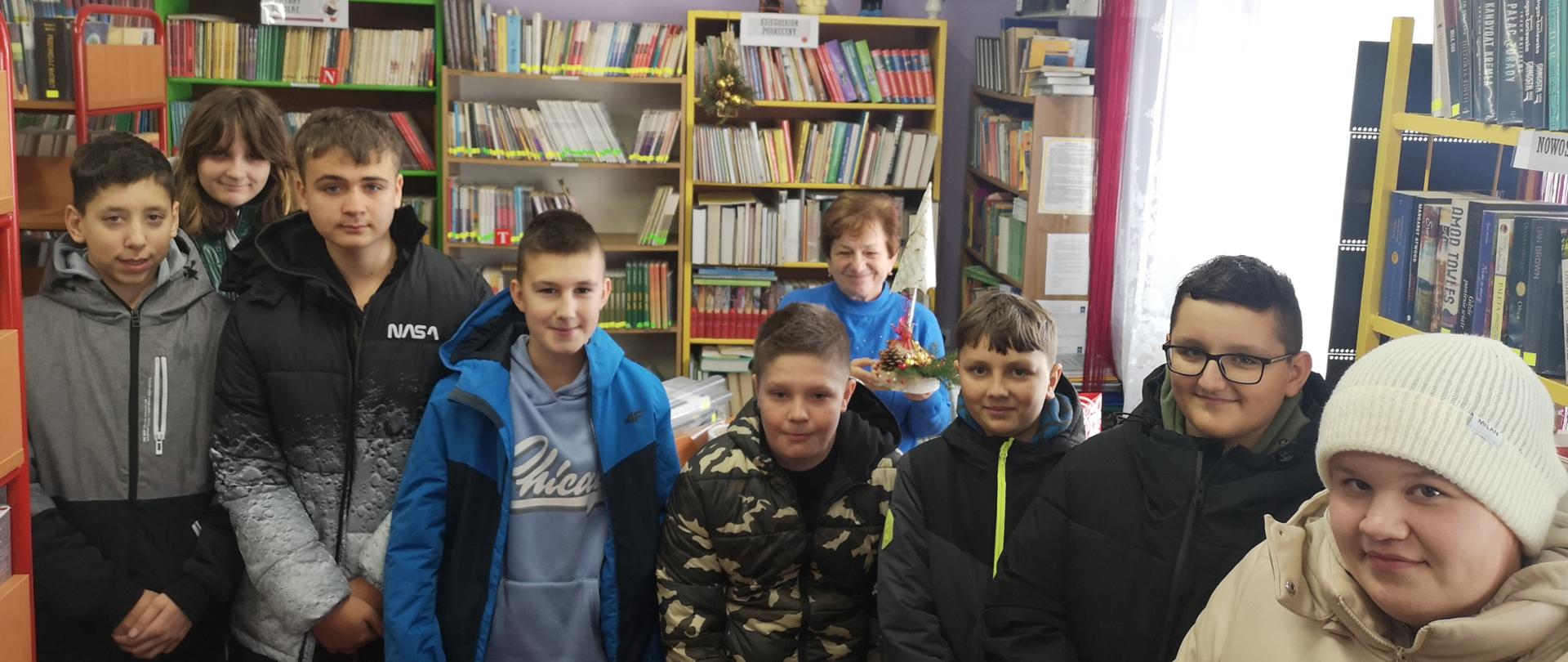 Uczniowie w bibliotece na tle regałów z książkami, w środku bibliotekarka z choinką