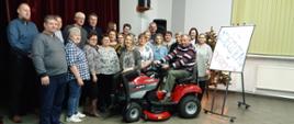Grupa mieszkańców Dębna pozująca do zdjęcia z nagrodą główną, jaką jest czerwony traktorek-kosiarka zdobytą w konkursie "Piękna Wieś Podkarpacka"