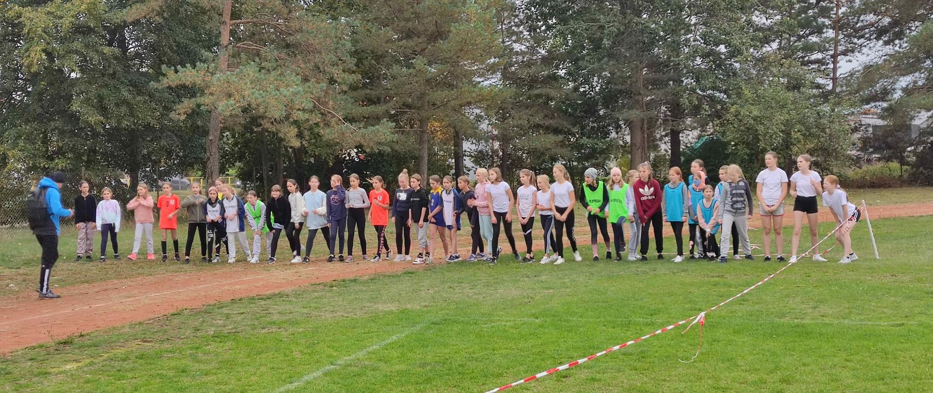 Zdjęcie przedstawia młodzież szkolną biorącą udział w wyścigu biegowym podczas inauguracji szkolnego roku sportowego pod patronatem Starostwa Powiatowego w Przasnyszu.