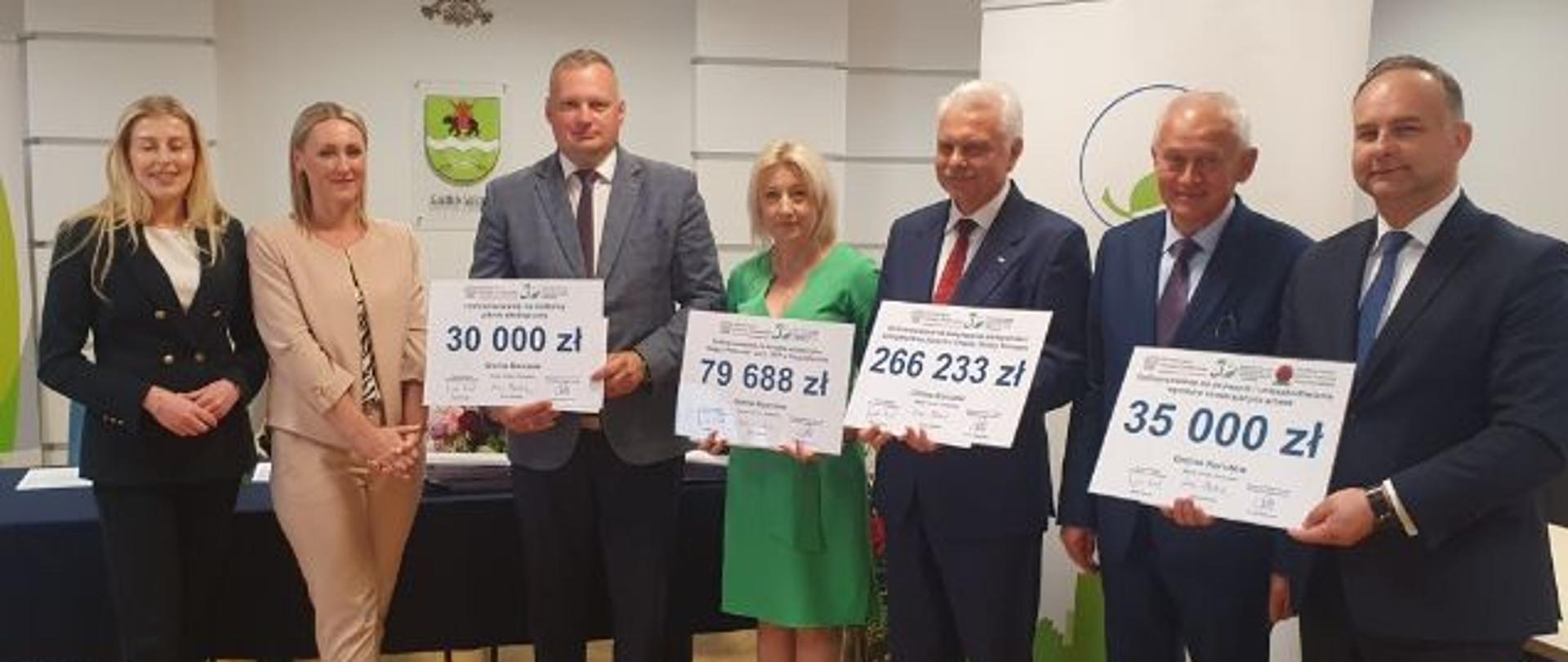 stoi siedem osób. W tle krzyż, godło Polski i logo Gminy Siedlce