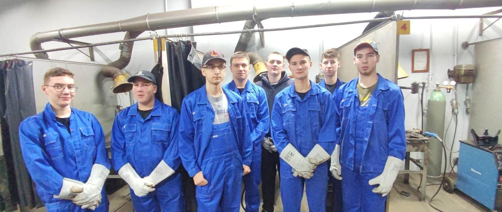 Kursanci pozują na tle warsztatów mechanicznych