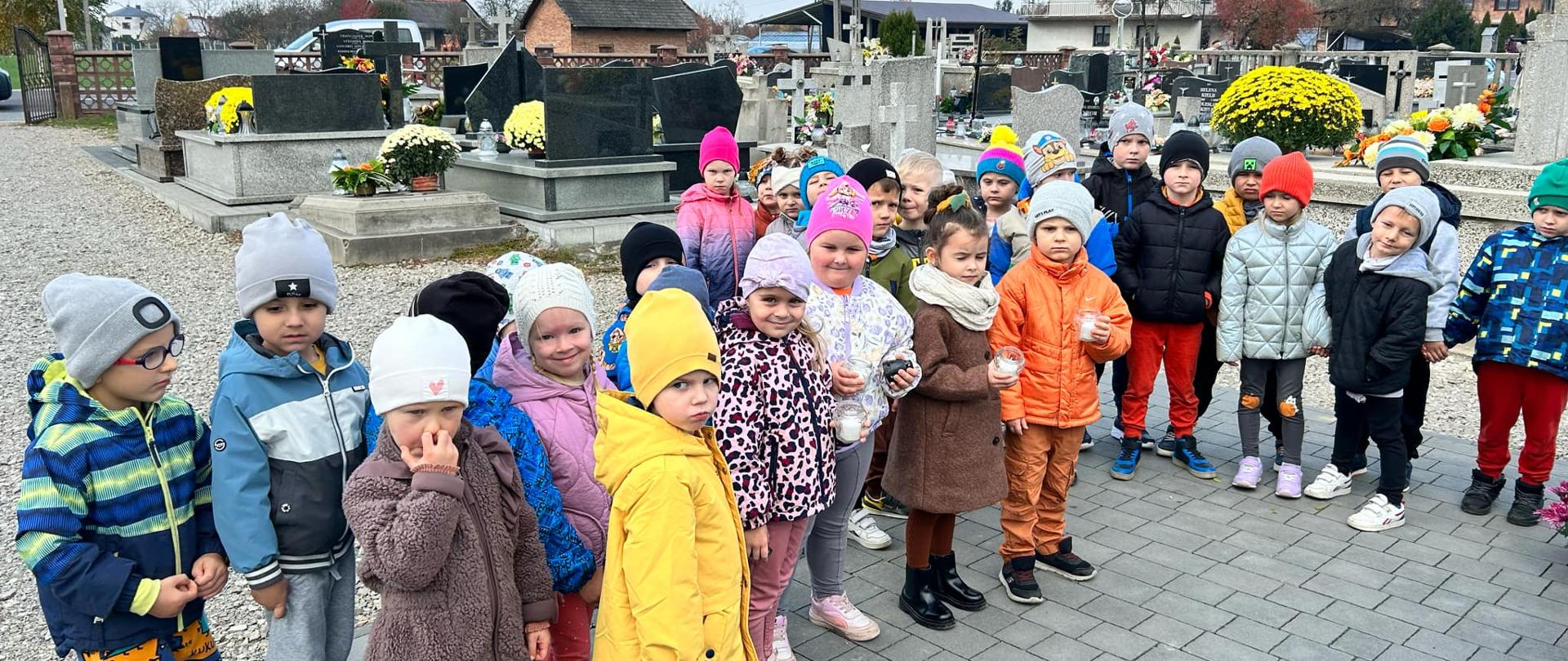 Dzieci odwiedzają groby zmarłych na pobliskim cmentarzu w nawiązaniu do Święta Zmarłych