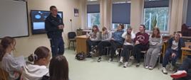 Uczniowie klasy ósmej siedzą w sali lekcyjnej na krzesłach ułożonych w okrąg, przed nimi pogadankę przeprowadzał pan policjant, wyświetlał prezentację na tablicy multimedialnej